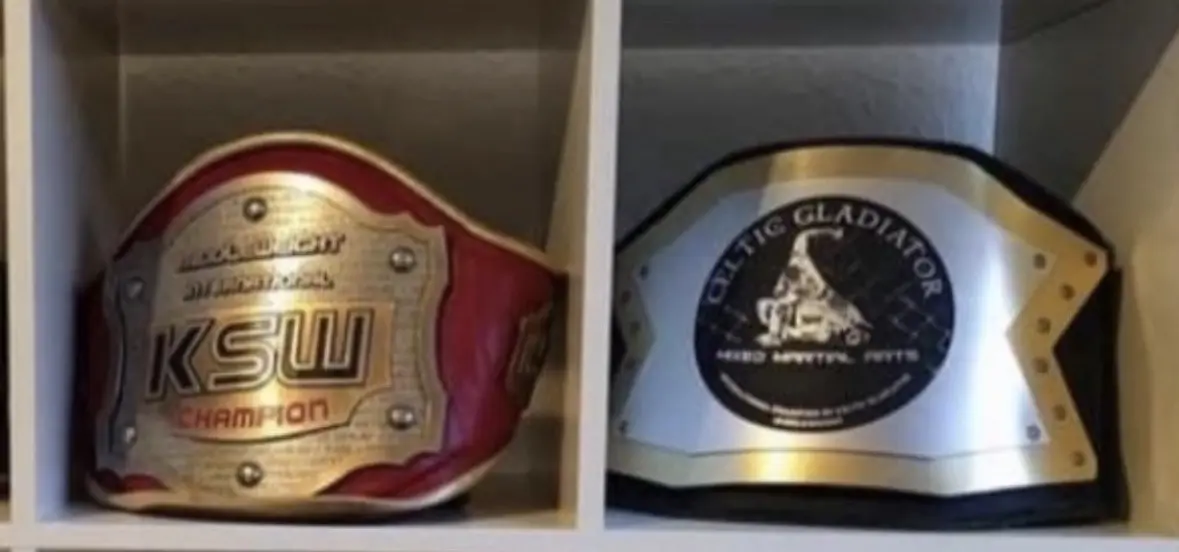 In einem Regal liegen zwei Gürtel: ein roter KSW-Championgürtel und ein silberner Gürtel mit der Aufschrift Baltic Gladiator.